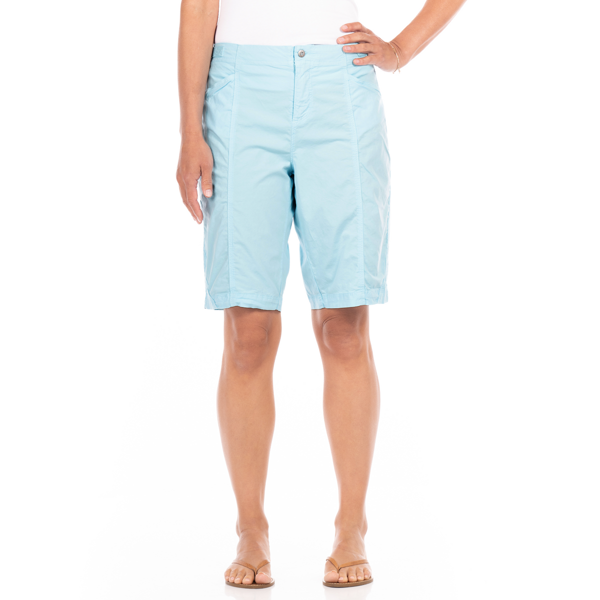 A person wearing light blue Cruiser Shorts from Fresh Produce Clothes, made from stretch broadcloth, paired with a white top and sandals, stands against a white background.