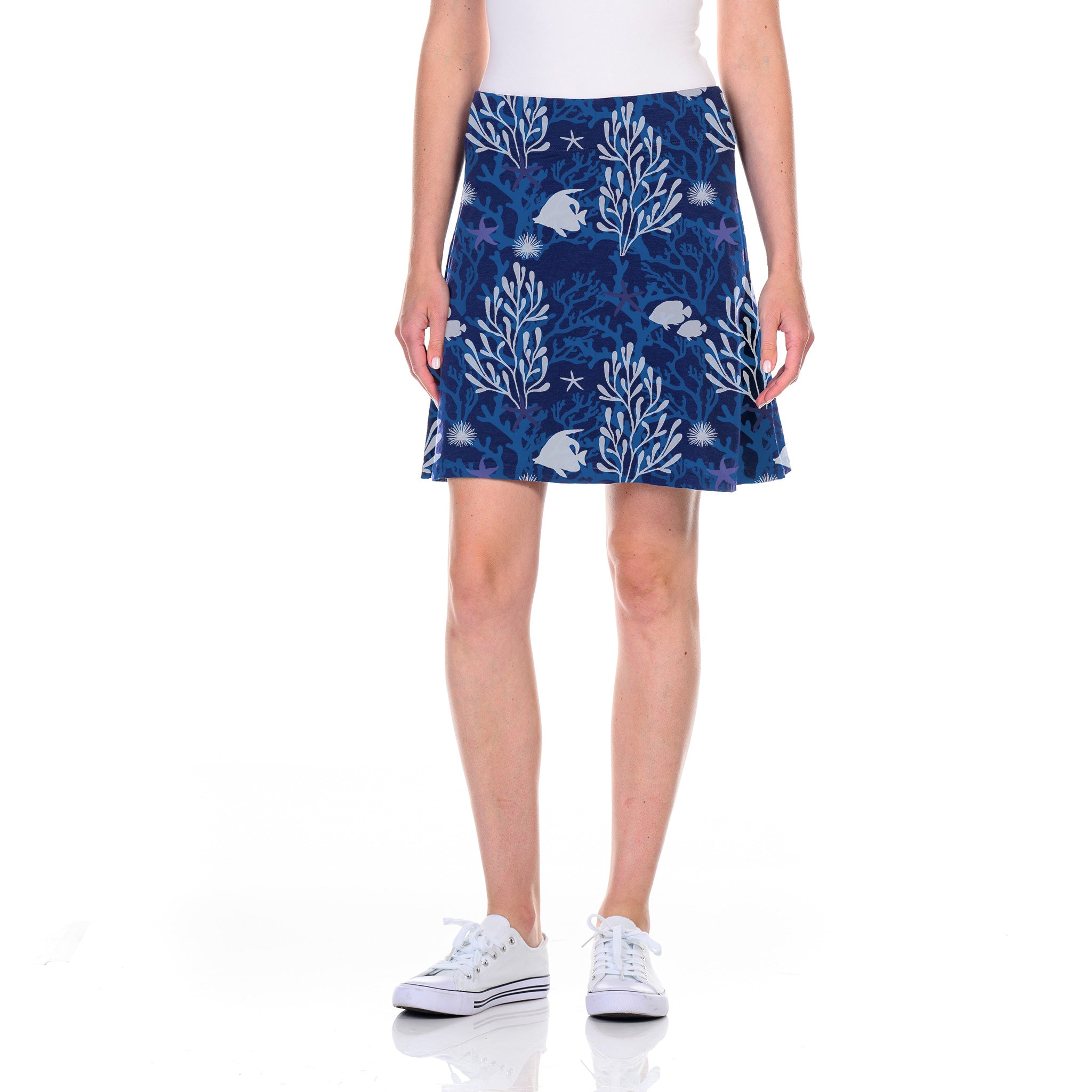 A person wearing the Coral Reef Marina Skirt from Fresh Produce Clothes, in South Beach Blue with an A-line silhouette and a charming floral and rabbit pattern, paired with a white top and white sneakers, stands against a plain white background. The skirt’s flattering waistband adds an elegant touch to the look.