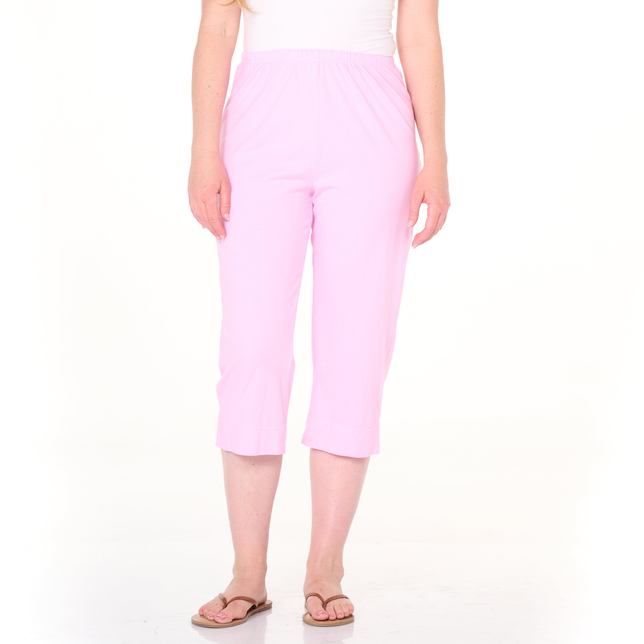 A person wearing Fresh Produce Clothes’ Jersey Capris Summer Colors in light pink, paired with a white sleeveless top and beige flip-flops, stands against a plain white background.