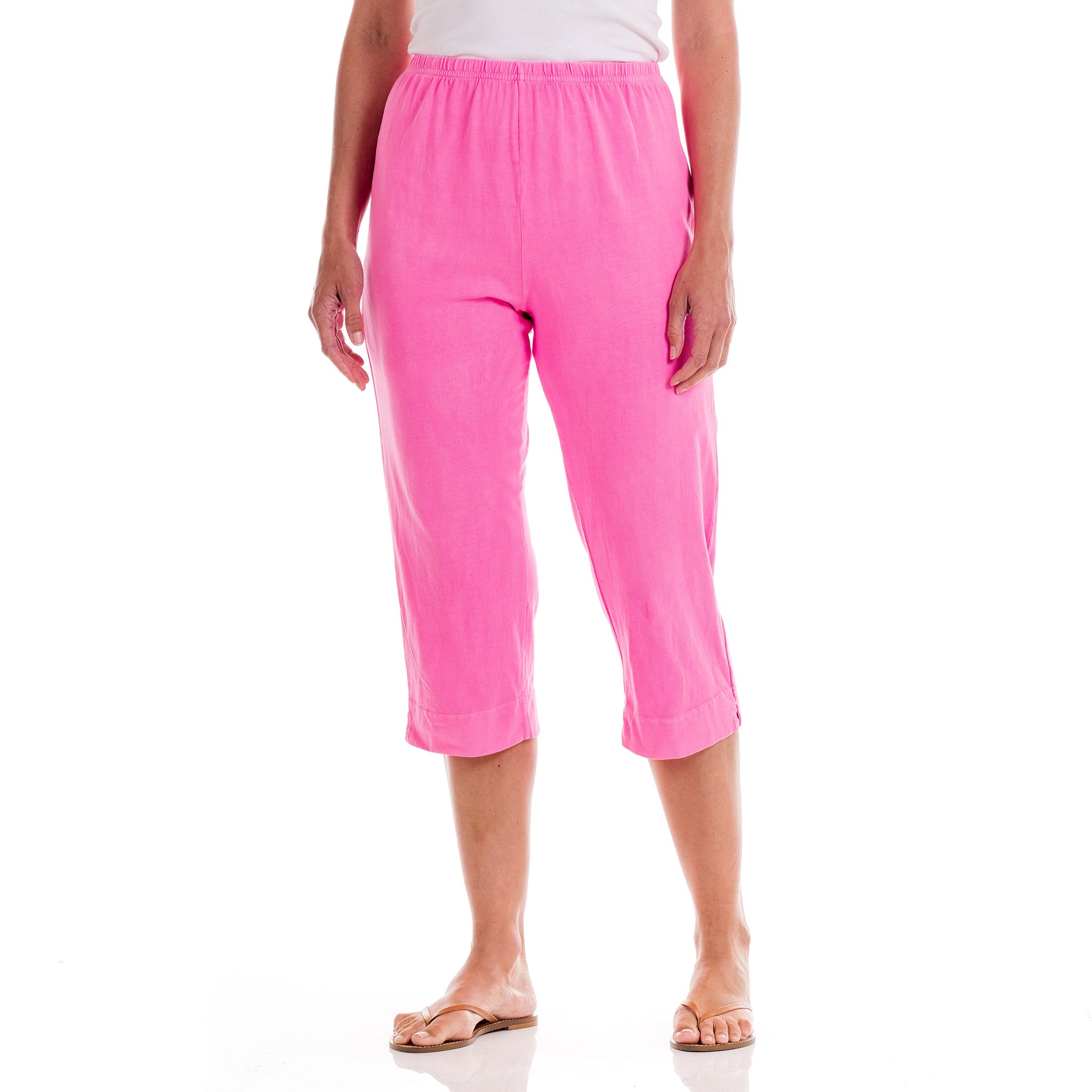 A person wears Fresh Produce Clothes Jersey Capris in bright pink from the clearance collection, featuring an elastic waistband, along with a white top and tan sandals. The background is plain white.