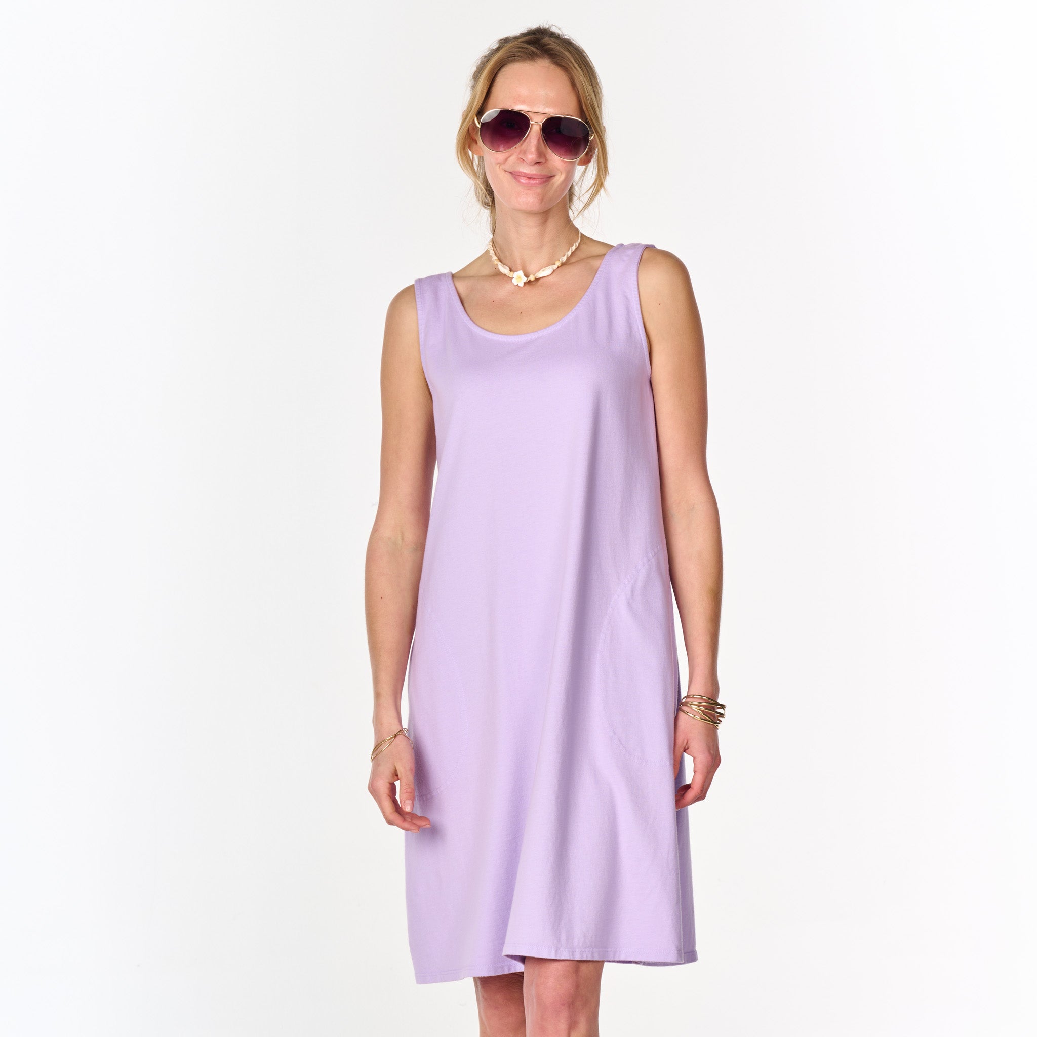 A woman stands and smiles against a plain white background, wearing the sleeveless lavender La Jolla Dress from Fresh Produce Clothes (Clearance), paired with sunglasses and jewelry.