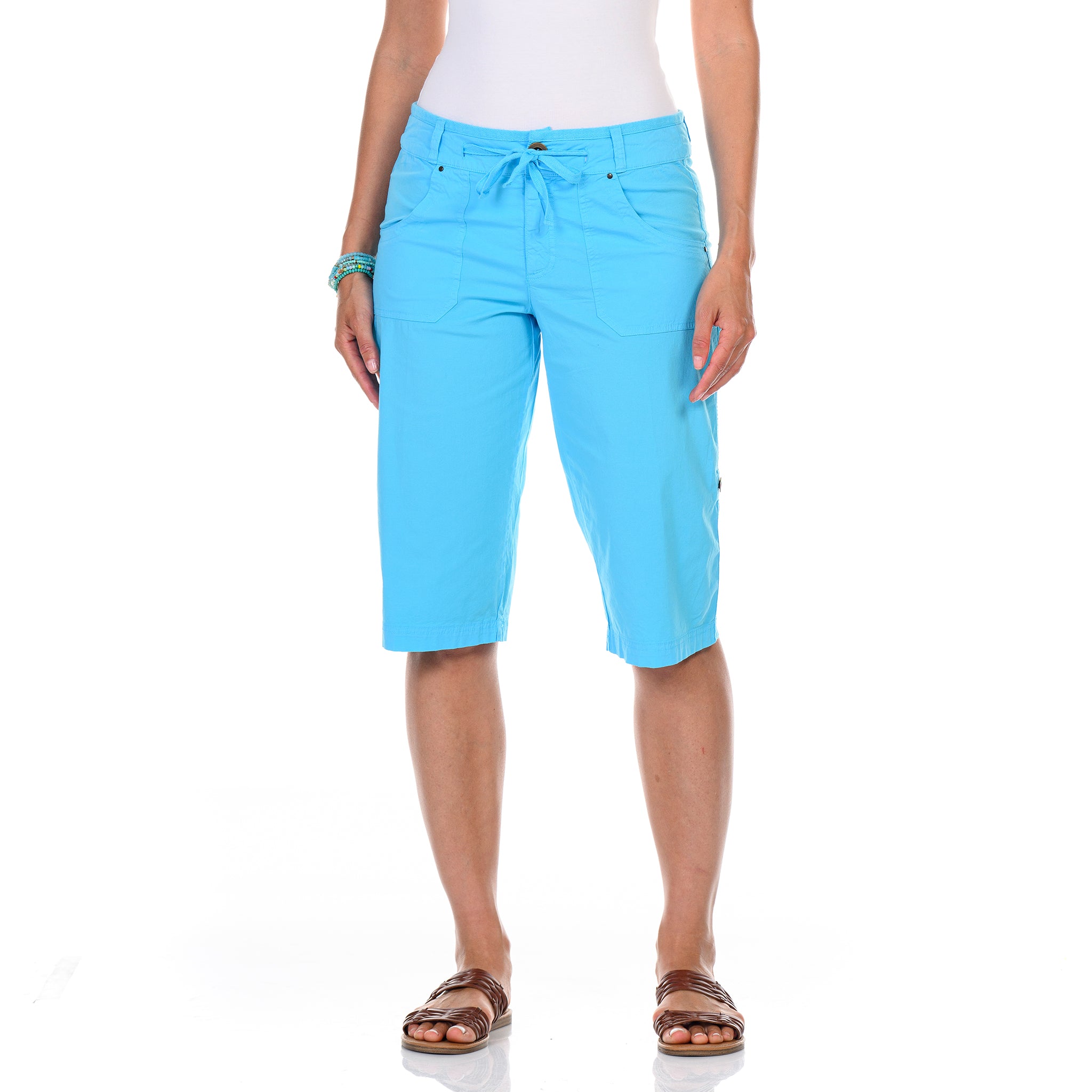 A person wearing Fresh Produce Clothes’ Safari Pedal Pushers Blue Fin in light blue, paired with a white top, brown sandals, and bracelets, stands against a white background.