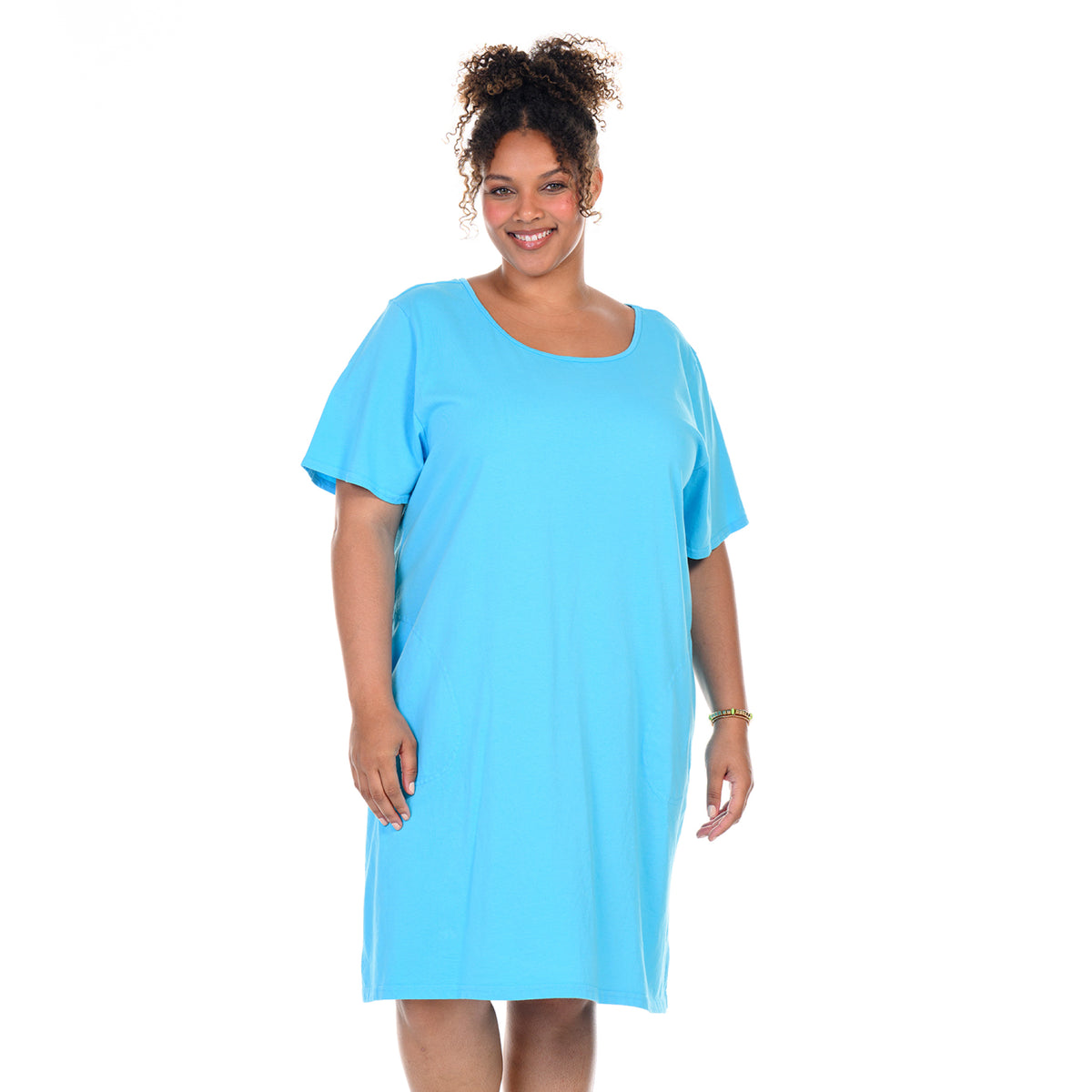 A woman with curly hair smiles while wearing the Sanibel Dress in Blue Fin, a loose-fitting, short-sleeve plus size t-shirt dress in soft cotton jersey from Fresh Produce Clothes. She stands against a plain white background.