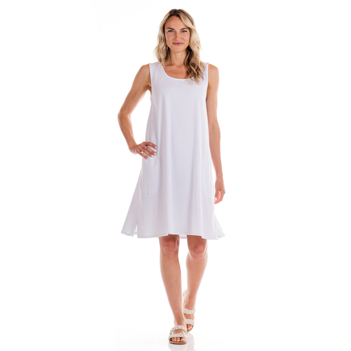 A woman stands and smiles, wearing the Fresh Produce Clothes sleeveless white cotton jersey Sun Dress and white sandals, posed against a plain white background.