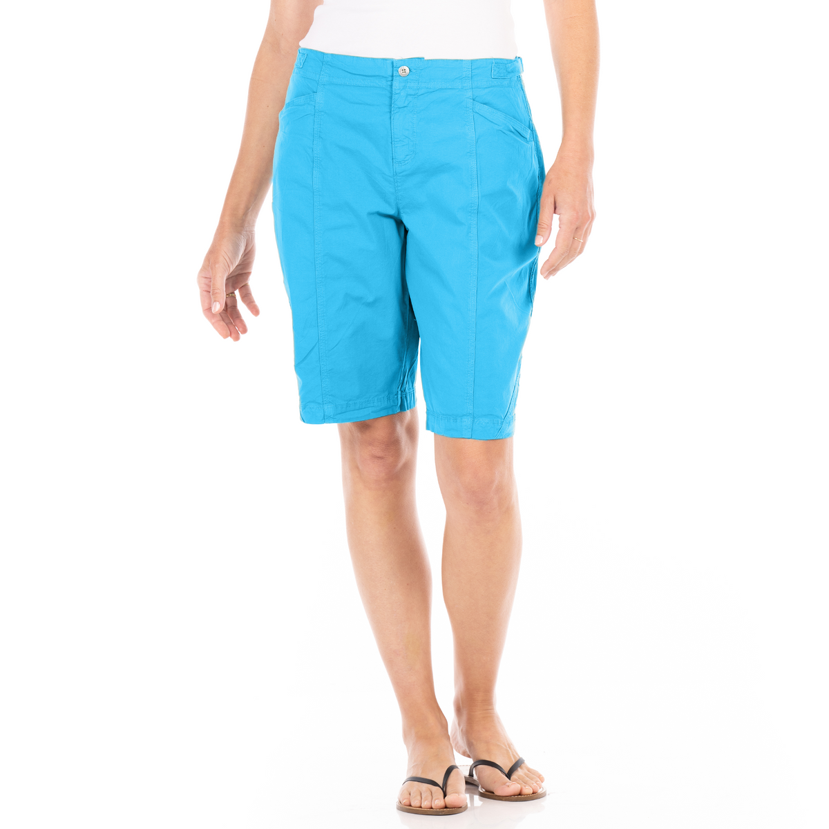 Wearing the Fresh Produce Clothes Cruiser Shorts in a vibrant bright blue, featuring coastal chic style and made from stretch broadcloth with a slimming front seam, a person pairs them with a white top and black flip-flops while standing against a white background.