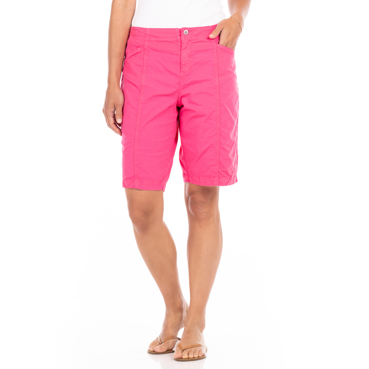 A person wearing vibrant pink Cruiser Shorts by Fresh Produce Clothes, crafted from stretch broadcloth, paired with a white top and beige flip-flops, stands against a white background.