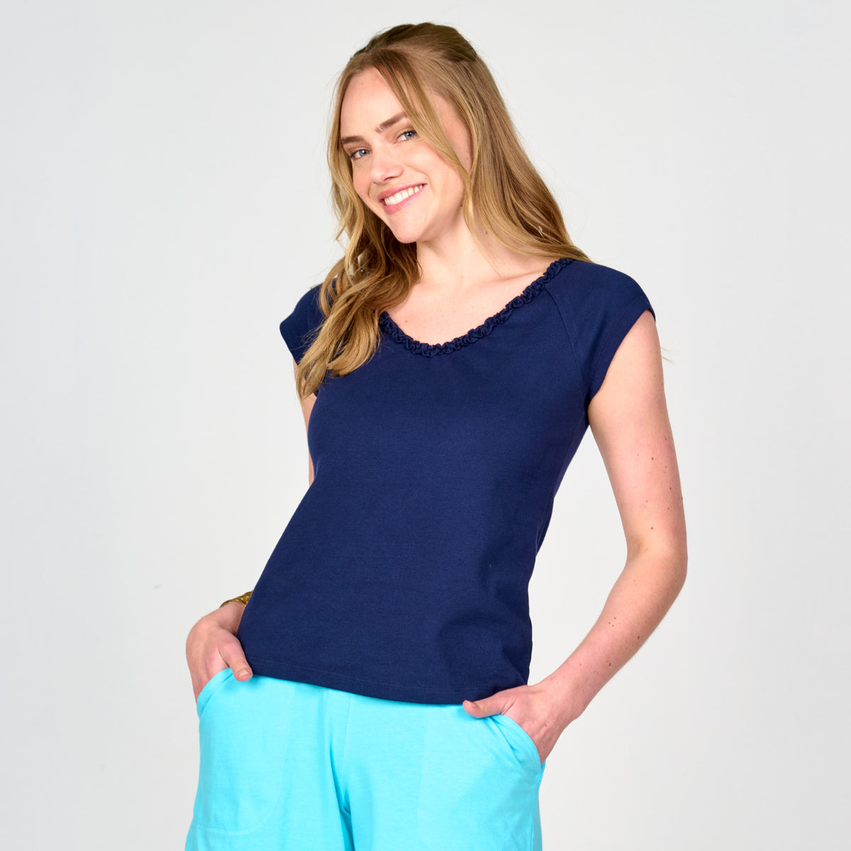 A woman wearing a navy blue Baby Rib Ruffle V Neck T with ruffled trim at the neckline and bright blue shorts.