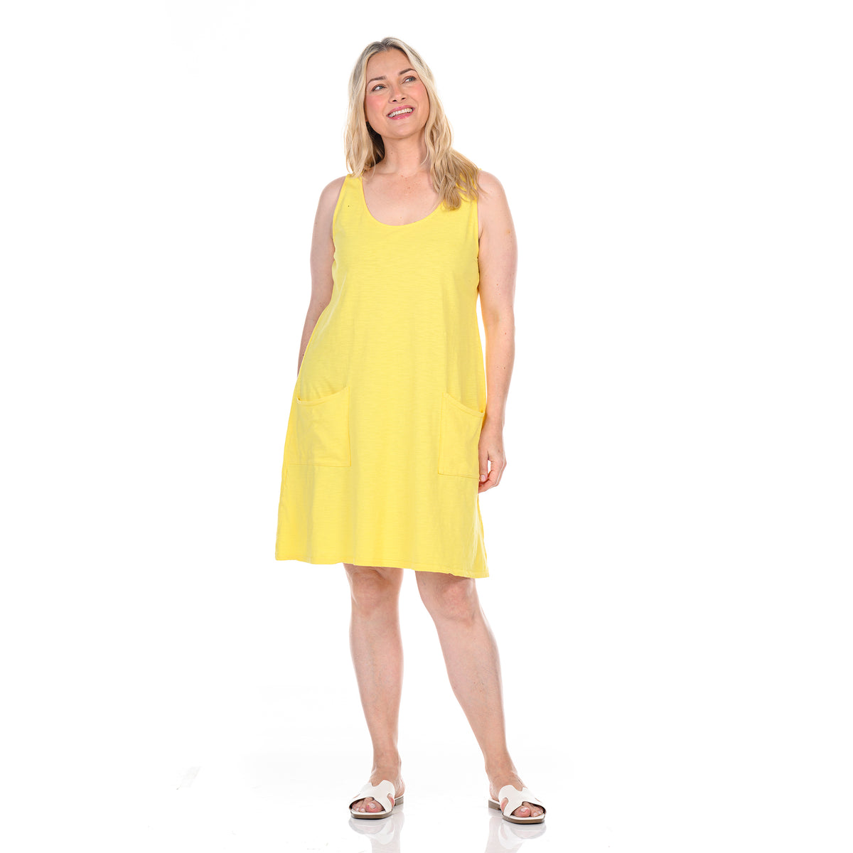 A smiling woman wears the Fresh Produce Clothes Drape Dress in a sleeveless yellow style with pockets, paired with white sandals, and stands against a plain white background. This plus size dress is available on clearance.