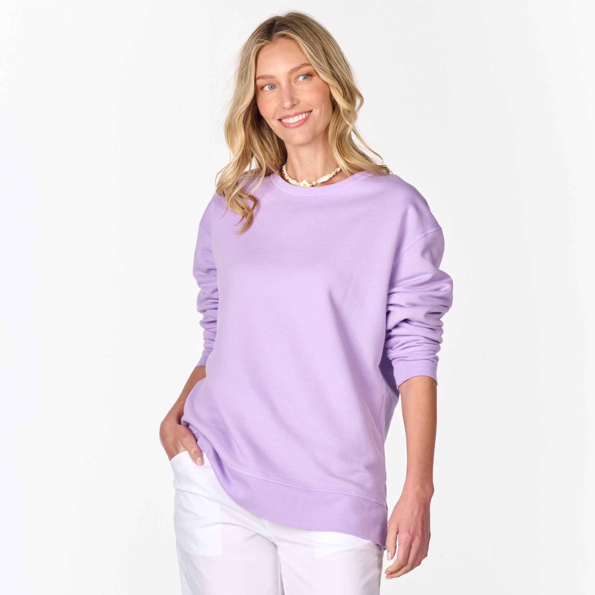 A woman with blonde hair smiles while wearing the Fresh Produce Clothes Easy Sweatshirt in light purple and white pants, standing against a plain white background.
