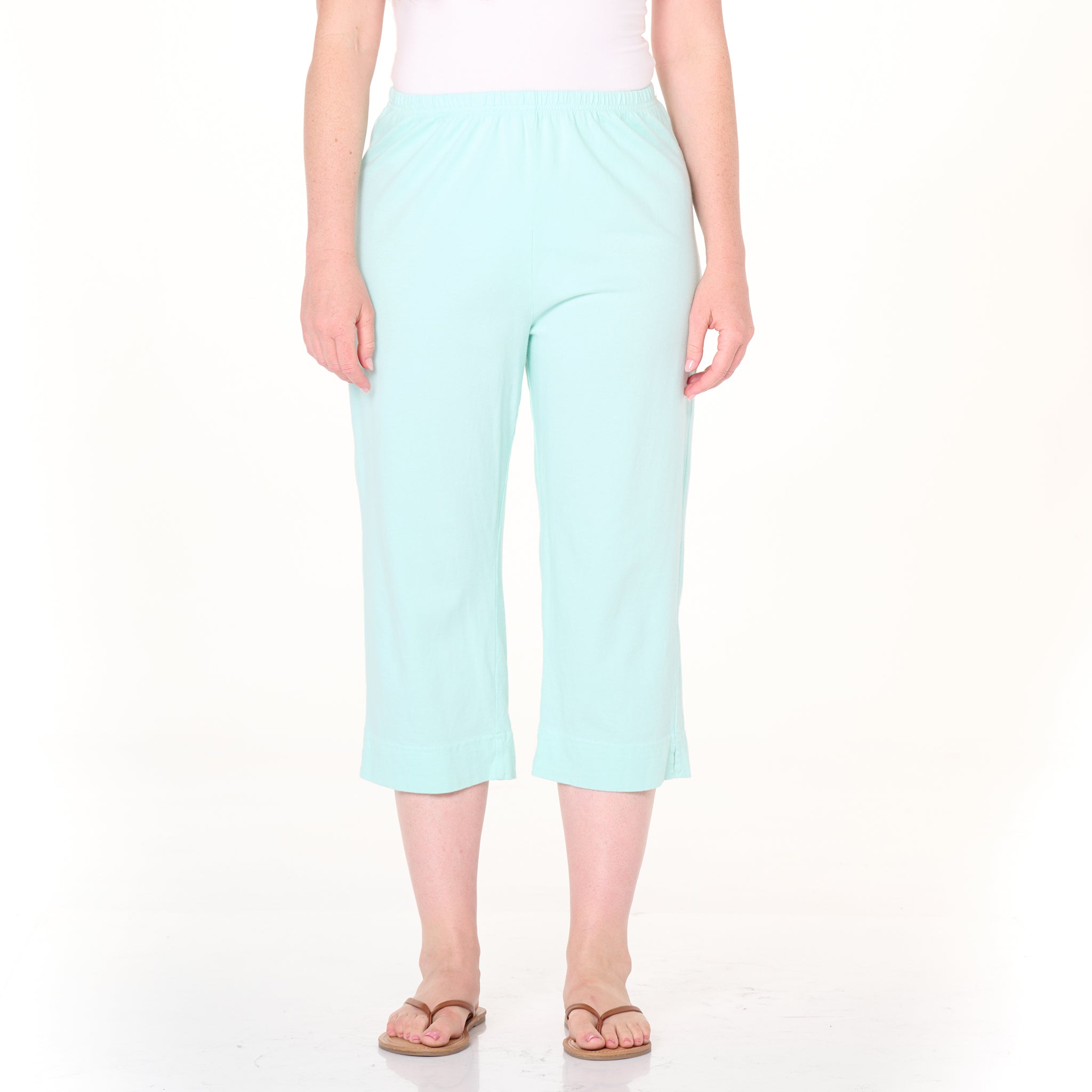 A person is shown from the waist down, standing facing forward against a plain white background, wearing light blue Fresh Produce Clothes Jersey Capris Summer Colors with an elastic waistband, paired with a white top and brown flip-flops.
