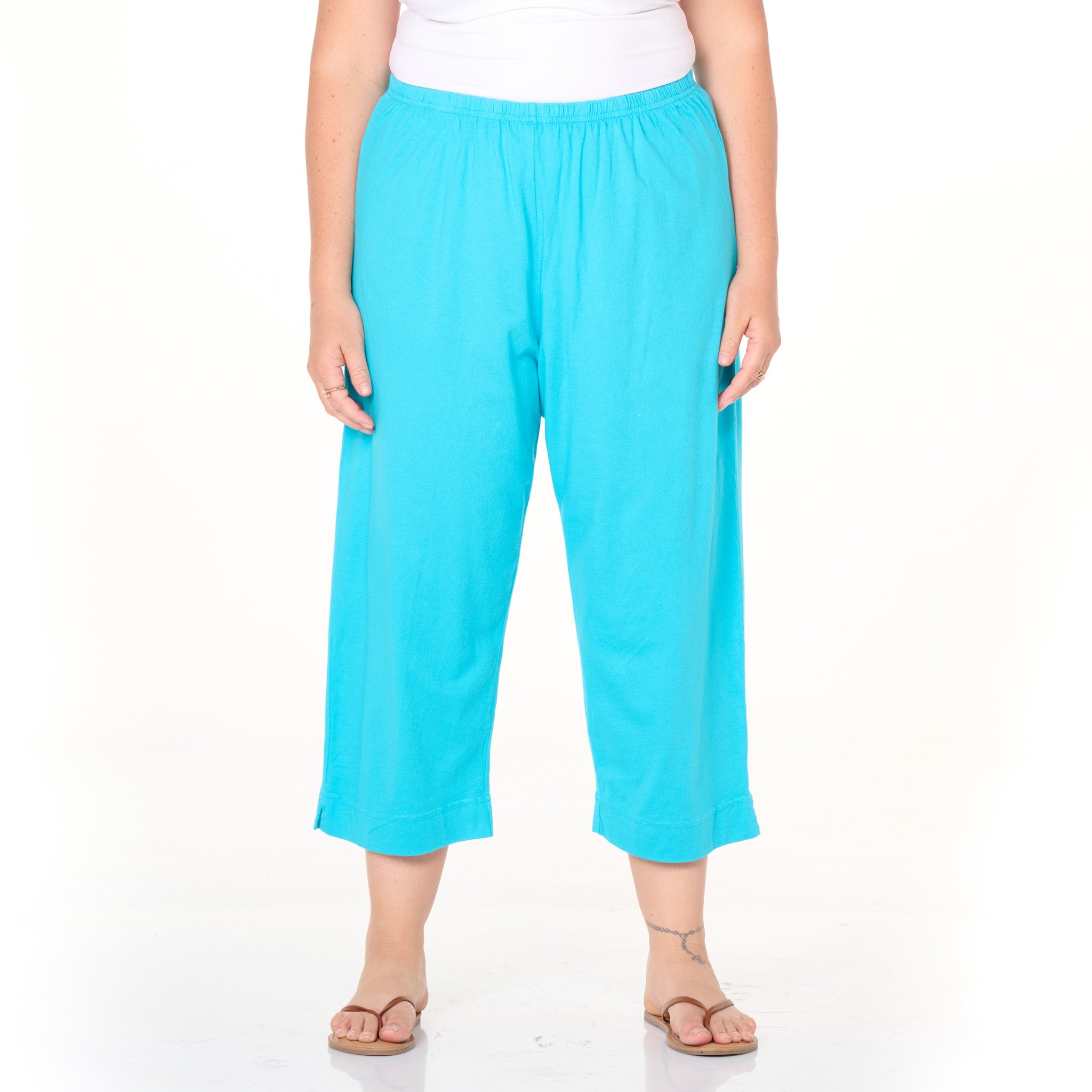 A person is shown wearing Fresh Produce Clothes’ Jersey Capris | Plus Size | Clearance in a loose, bright turquoise style with an elastic waistband, paired with a white top and tan flip-flops. The individual stands against a plain white background, with their face not visible in the image.