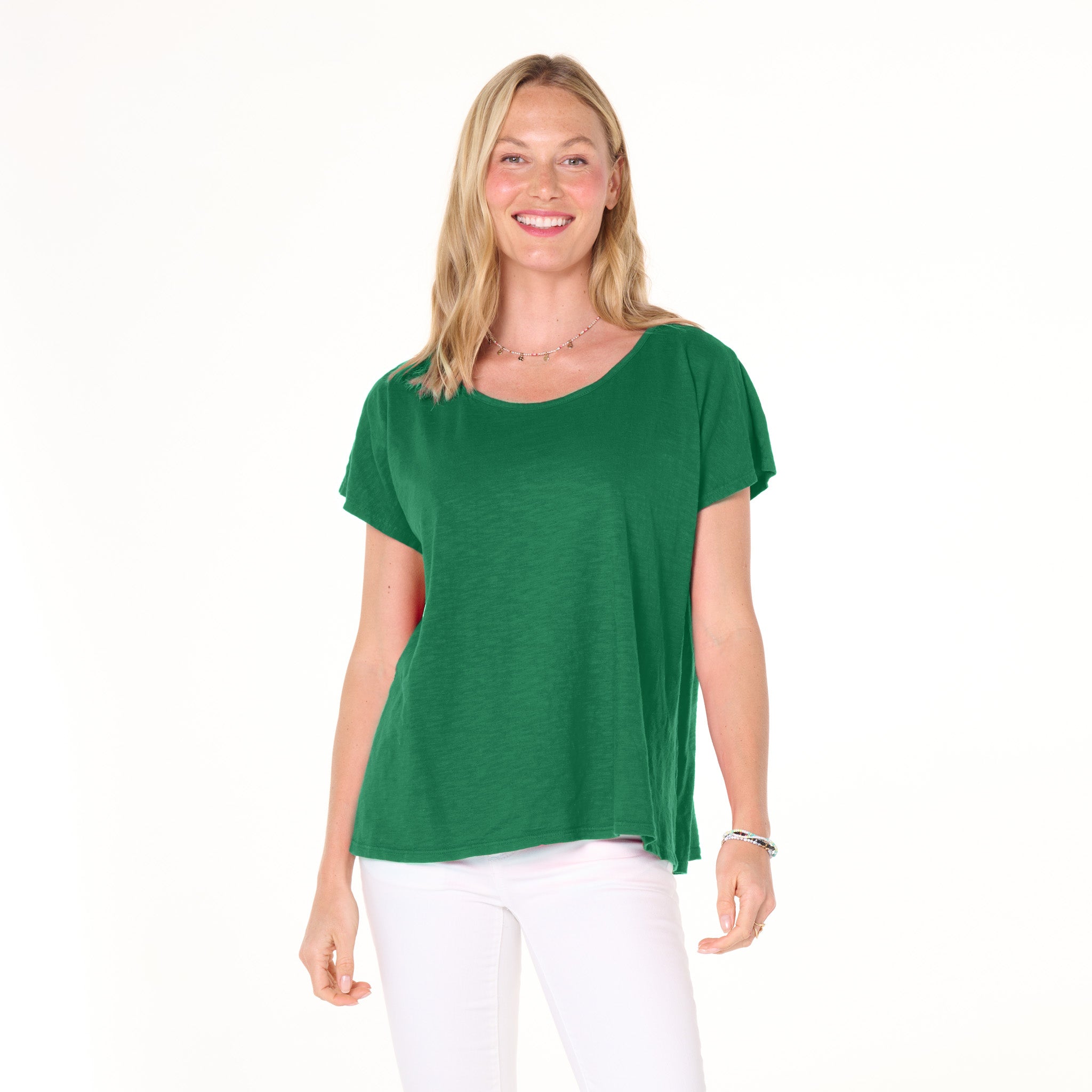 Smiling woman wearing the Fresh Produce Clothes Keepsake T - 2025 Fall Colors in green, paired with white pants, standing against a plain white background.