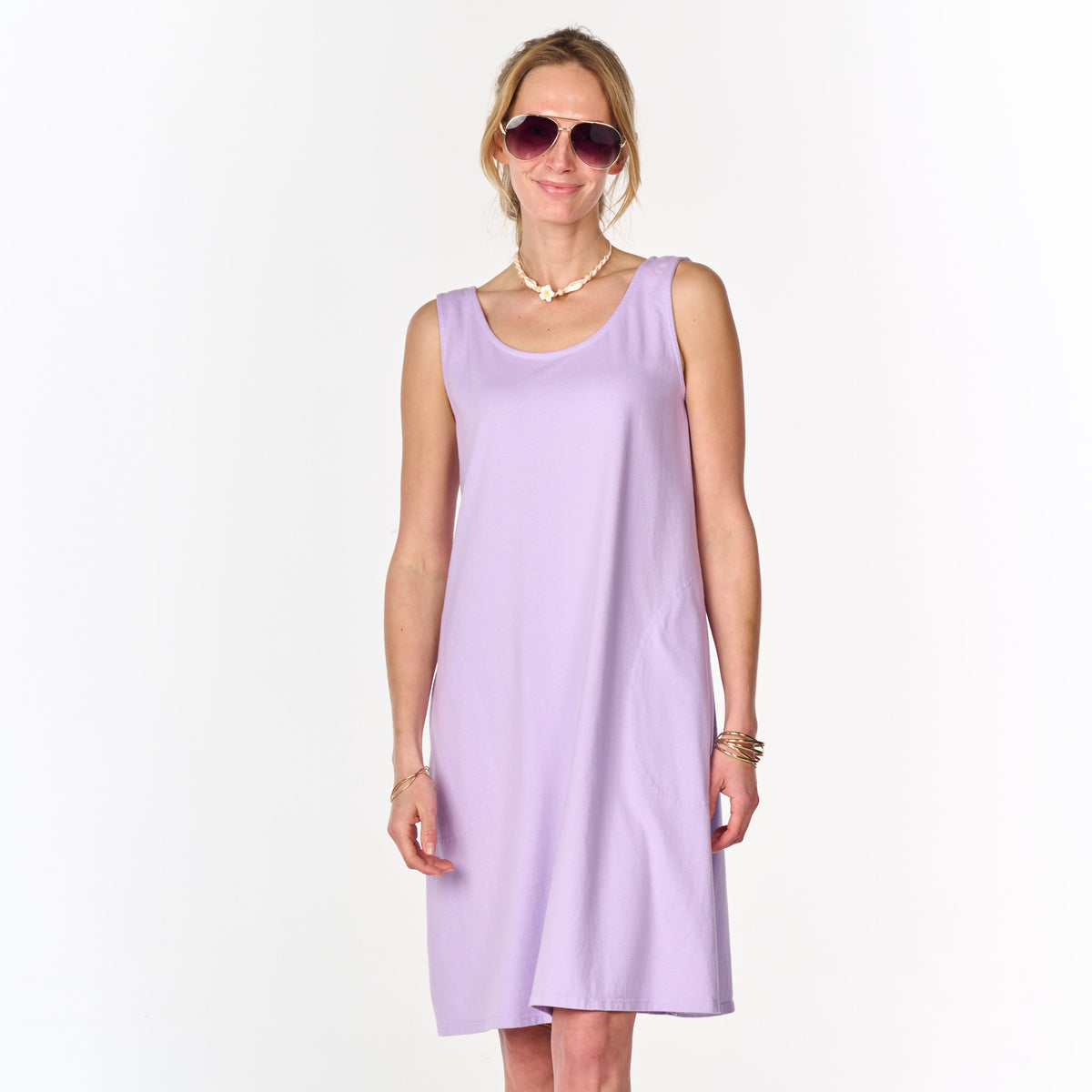 A woman stands and smiles against a plain white background, wearing the sleeveless lavender La Jolla Dress from Fresh Produce Clothes (Clearance), paired with sunglasses and jewelry.