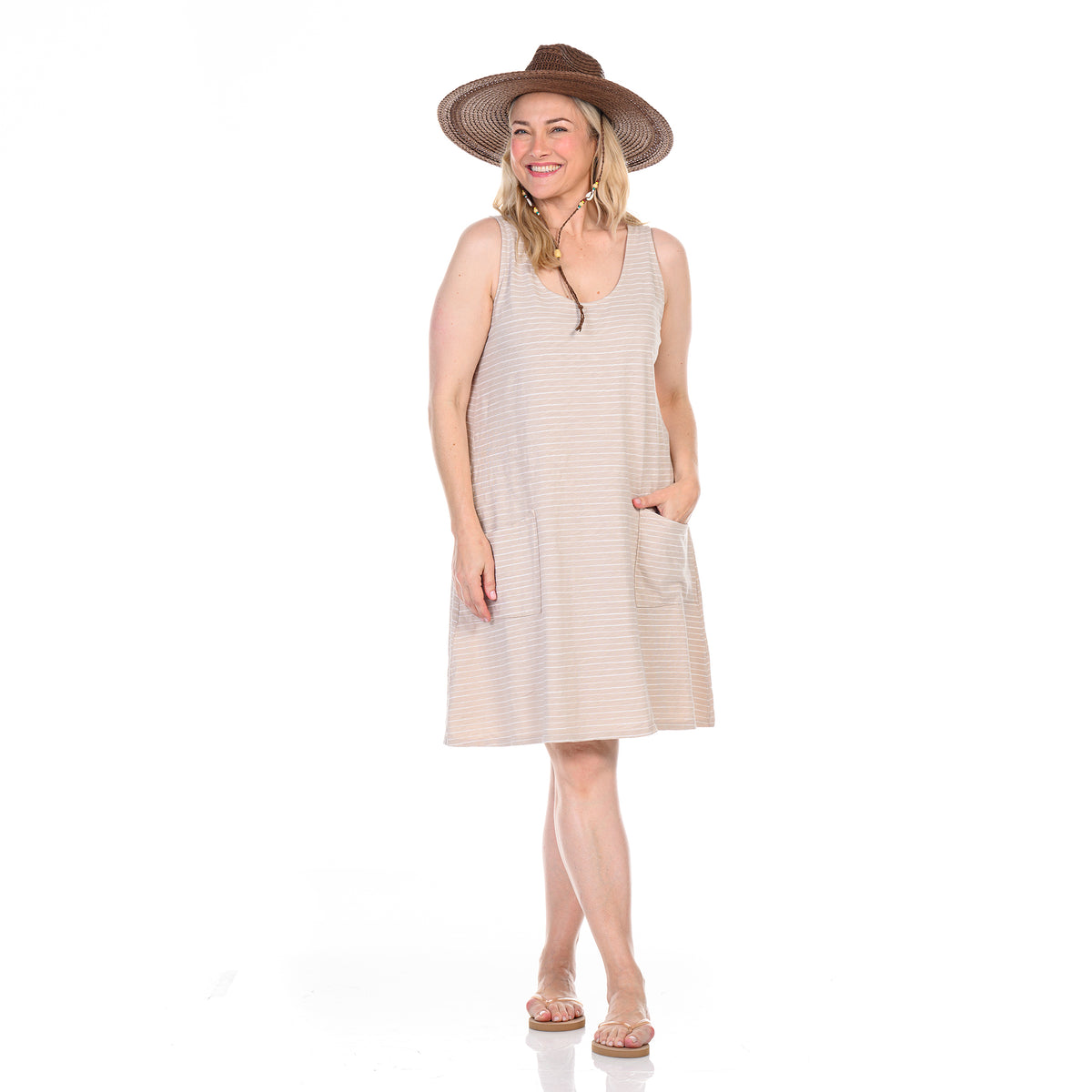 A smiling woman in the Ocean Stripe Drape Dress | Plus Size by Fresh Produce Clothes, with a brown wide-brimmed hat and sandals, stands with one hand in her pocket against a white background.