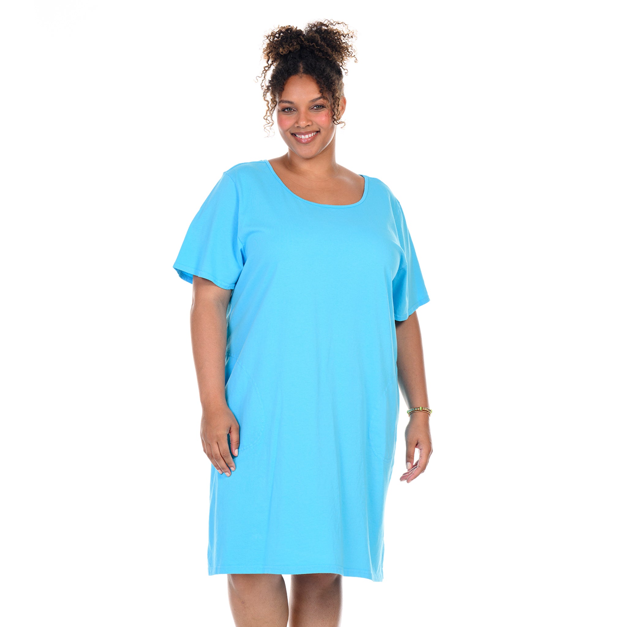 A woman with curly hair smiles while wearing the Sanibel Dress in Blue Fin, a loose-fitting, short-sleeve plus size t-shirt dress in soft cotton jersey from Fresh Produce Clothes. She stands against a plain white background.