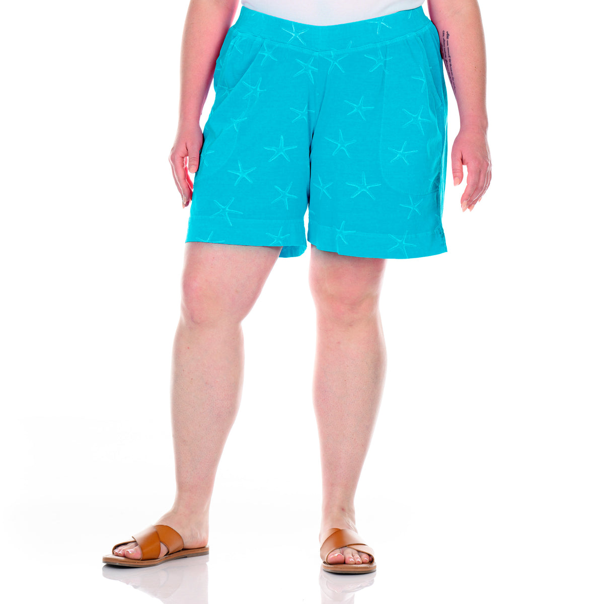 A person stands against a white background wearing Fresh Produce Clothes’ Sea Star 7″ Key Largo Shorts in bright turquoise—plus size clearance shorts crafted from 100% cotton with a subtle starfish print—paired with a white top and tan sandals.