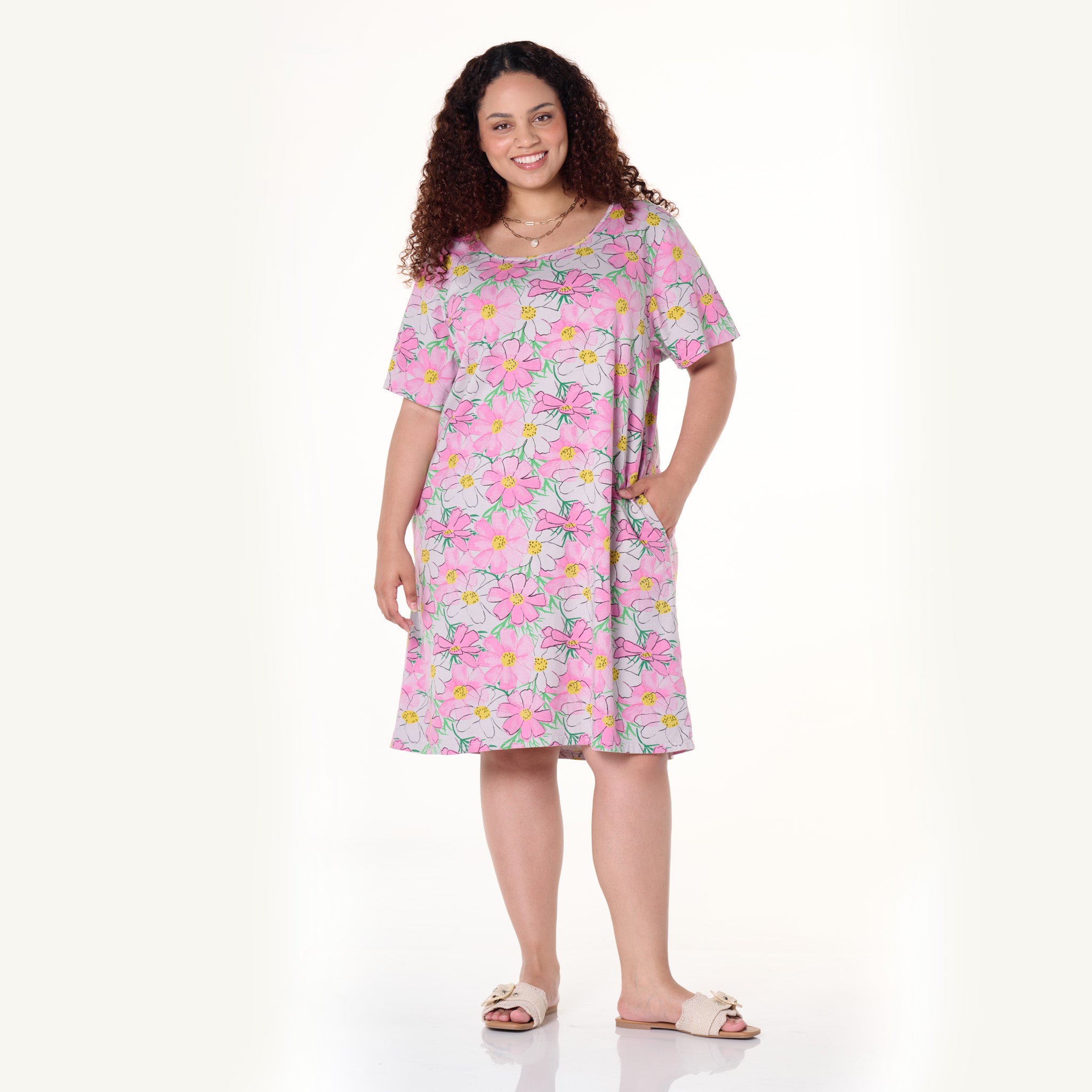 Smiling woman with curly hair wearing the Fresh Produce Clothes Spring Day Sanibel Dress in plus size and sandals, standing with one hand in her pocket against a plain, light background.