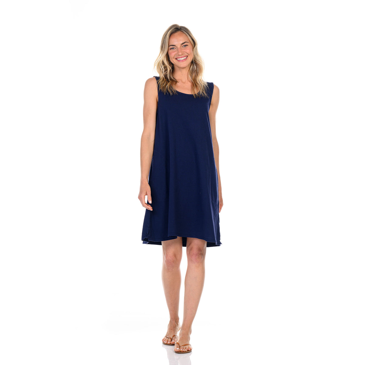 A woman with blonde hair, wearing the Fresh Produce Clothes Sun Dress—a sleeveless navy blue cotton jersey style—and sandals, stands smiling against a plain white background.
