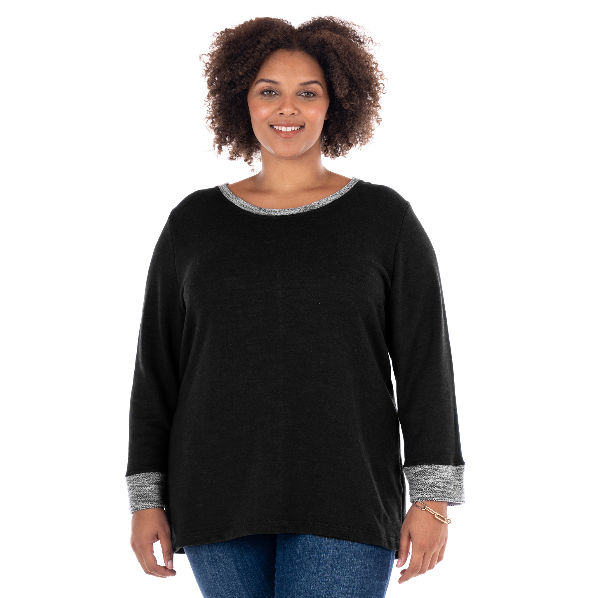 A woman with curly hair, wearing the Fresh Produce Clothes Sunset Sweatshirt in plus size—crafted from soft French terry cotton with gray trim at the collar and cuffs—in a relaxed black long-sleeve fit, pairs it with blue jeans and smiles at the camera against a white background.