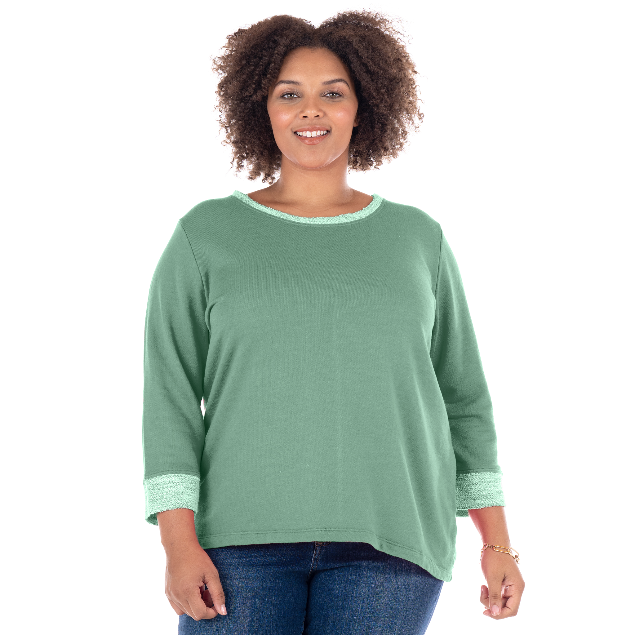 A woman with curly hair, smiling and standing against a plain white background, is wearing the Fresh Produce Clothes Sunset Sweatshirt in green (Plus Size, Clearance), made from soft French terry cotton, paired with blue jeans.