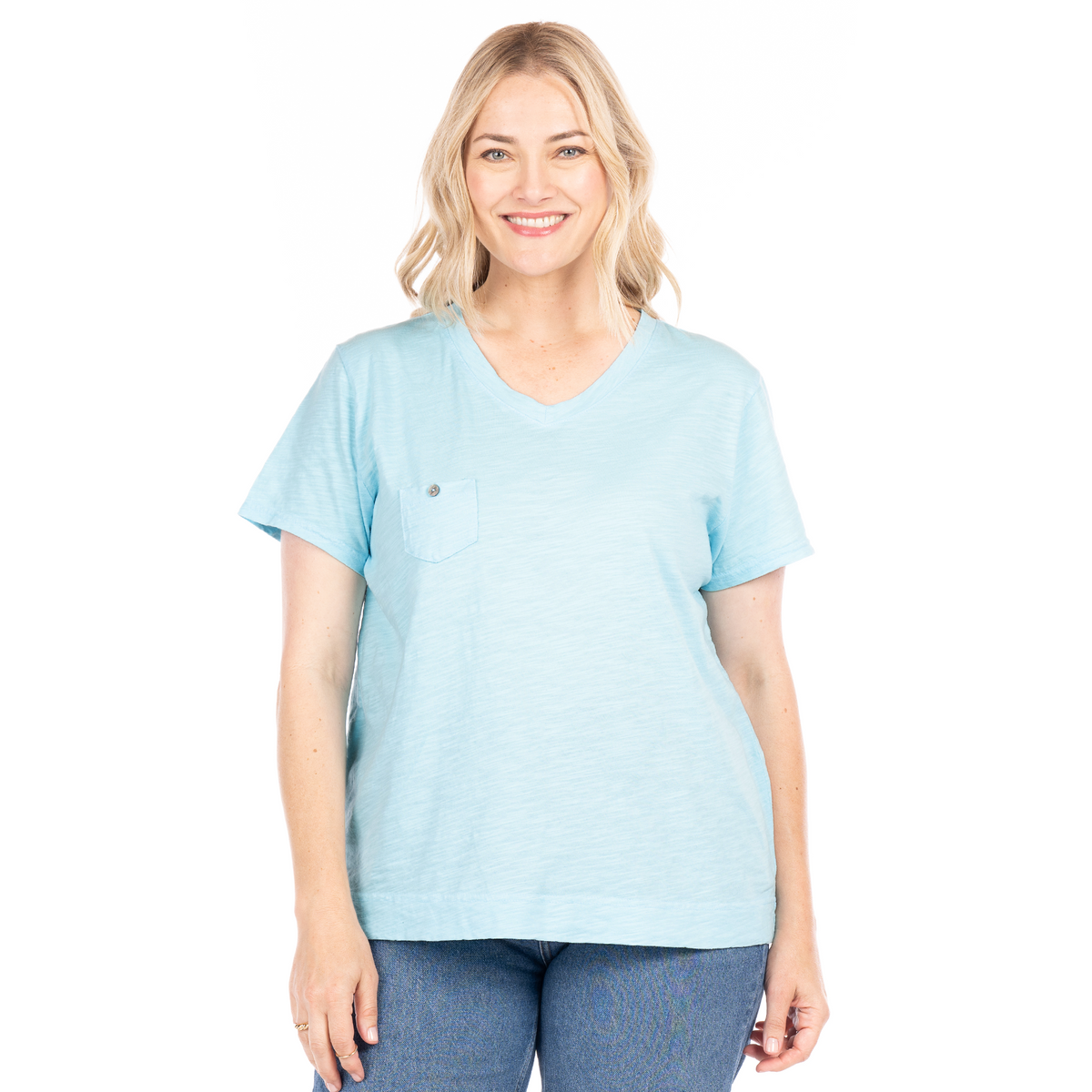 A woman with blonde hair, dressed in a light blue Fresh Produce Clothes Heritage Logo Fem T | Plus Size—a cotton slub V-neck tee with a chest pocket—pairs it with blue jeans and smiles at the camera against a white background.